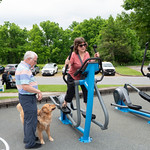 Woman using an elliptical while older man and dog watch nearby.