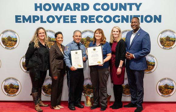 A photo of County Executive Calvin Ball and Howard County Government leaders with the County's 2025 Employee of the Year Genevieve LaPorte from the Howard County Police Department.
