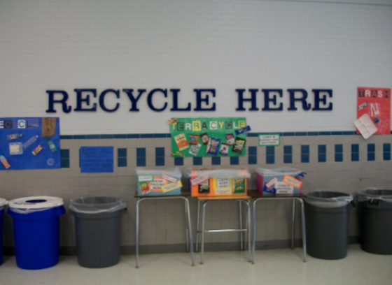 waste containers against wall in cafeteria with the words "recycle here" above them