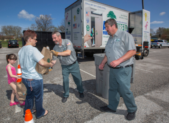 adult handing paper bag of documents to employee to be shredded at County event