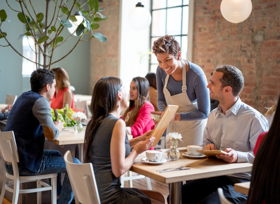 Waitress standing at a table in a restaurant taking an order from two adults.