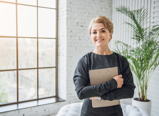 female holding folder standing in a white room with a window