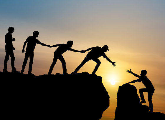 Silhouette of people helping others up a steep mountain
