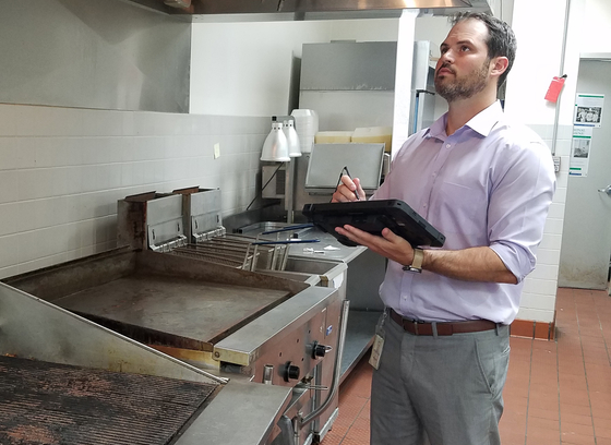 A health inspector examining a fume hood in a restaurant kitchen for cleanliness.